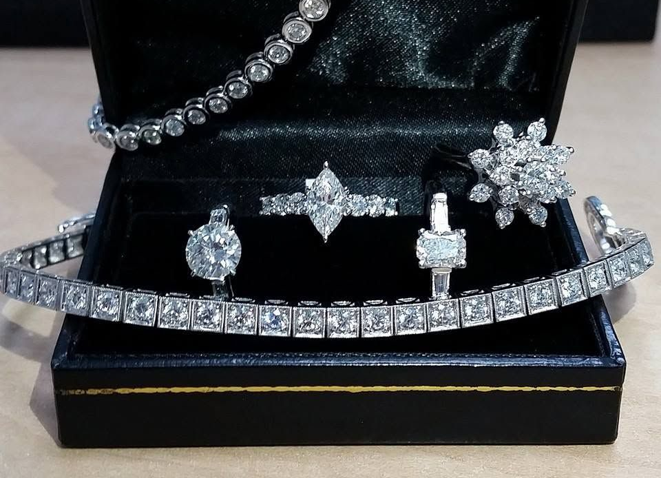 Black jewelry box displaying a diamond necklace, bracelet, and matching rings on a beige surface