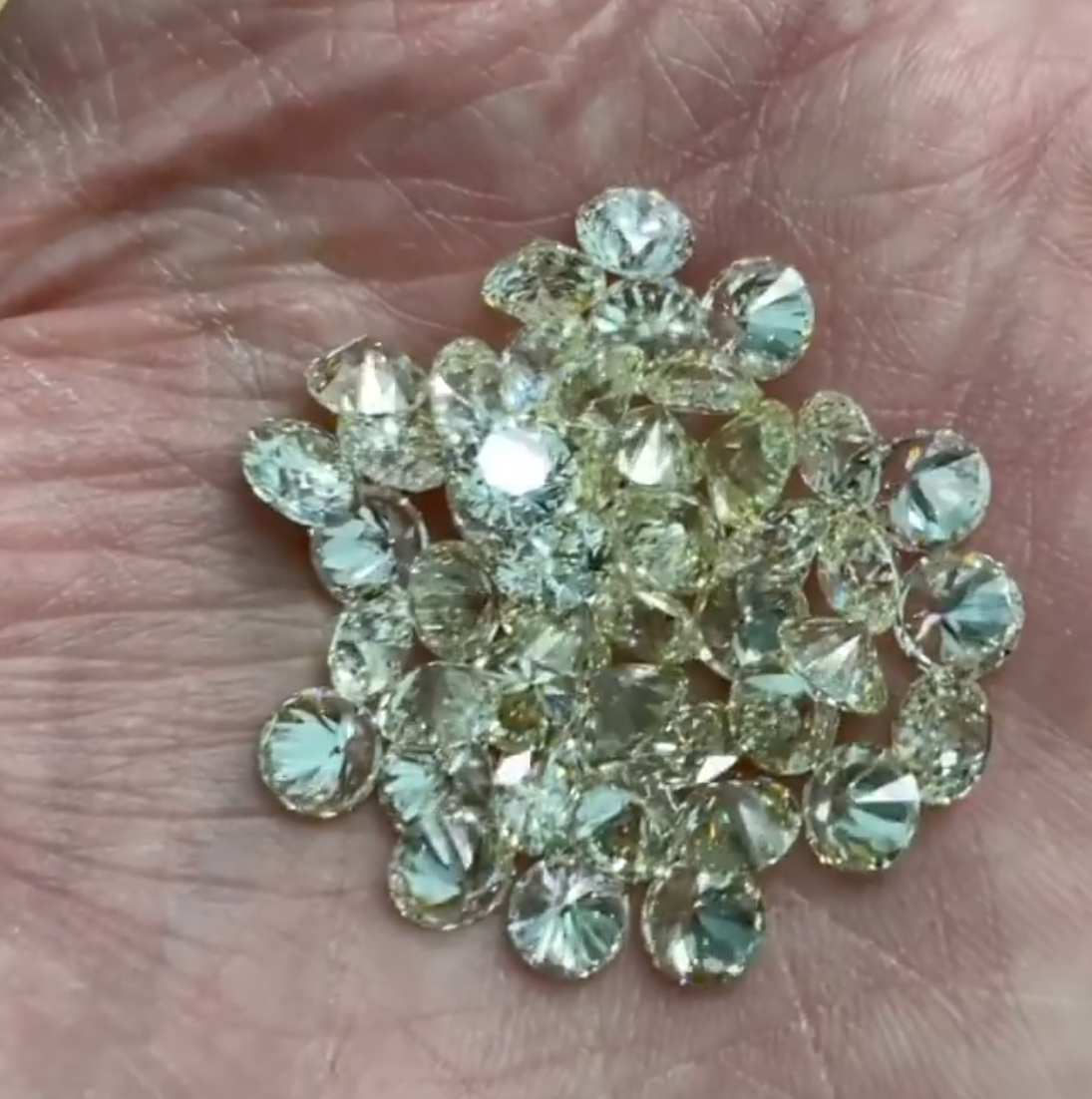 Small cluster of pale yellow and clear faceted gemstones resting on a palm