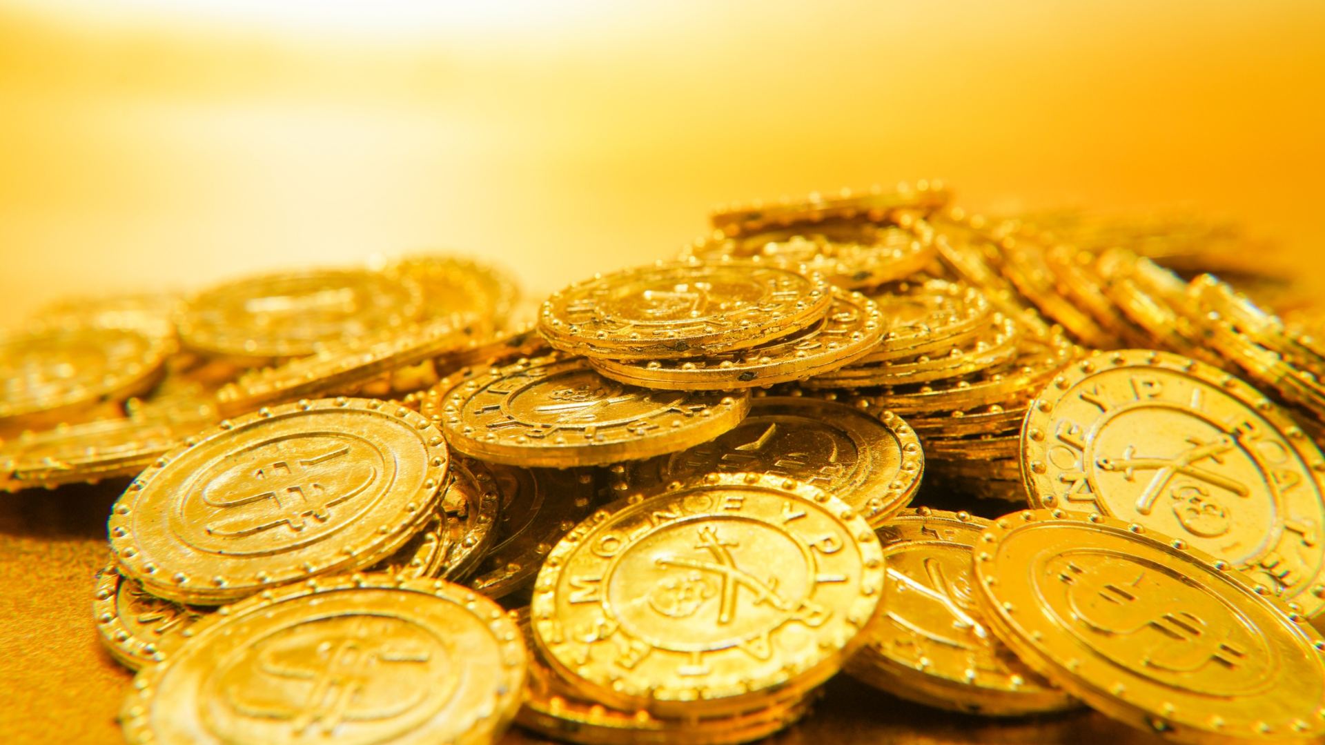 Pile of shiny gold coins stacked on a warm yellow background