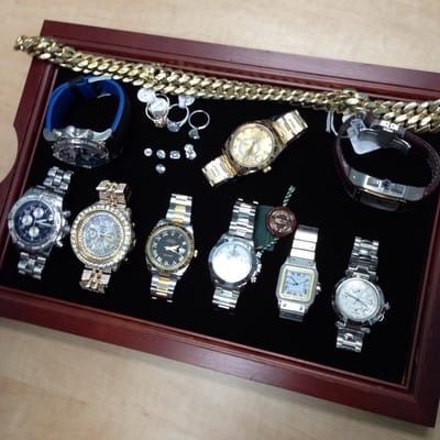 A wooden display box with several wristwatches and jewelry arranged on black velvet.