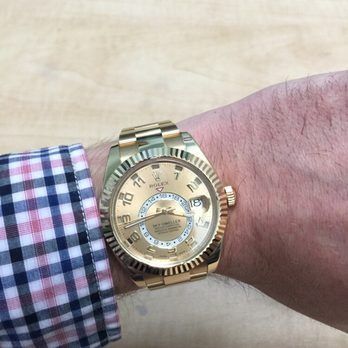 Gold wristwatch on a person’s wrist with a checkered shirt cuff against a light background