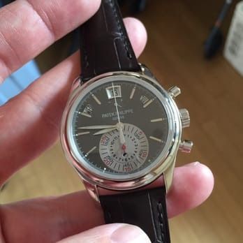 Close-up of a silver wristwatch with a black leather strap held in a hand.