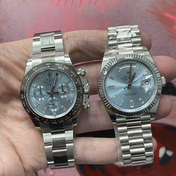 Two silver wristwatches held in a hand, one dark-faced chronograph and one light-faced date watch.