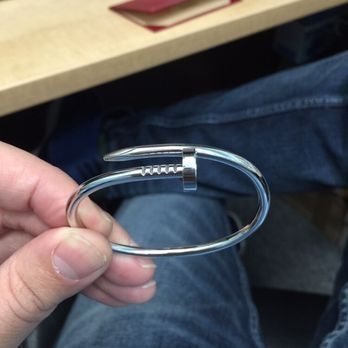 Hand holding a silver metal bracelet with a clasp, resting near jeans and a desk edge.