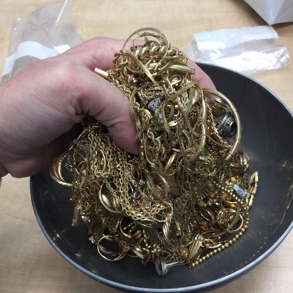 Hand holding a bowl full of tangled gold-colored chains and jewelry scraps