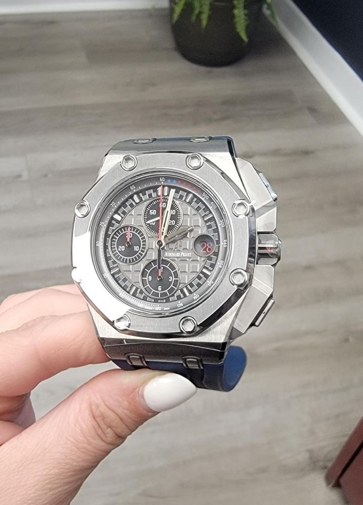 Close-up of a silver luxury wristwatch with a skeleton dial, held in a hand indoors.