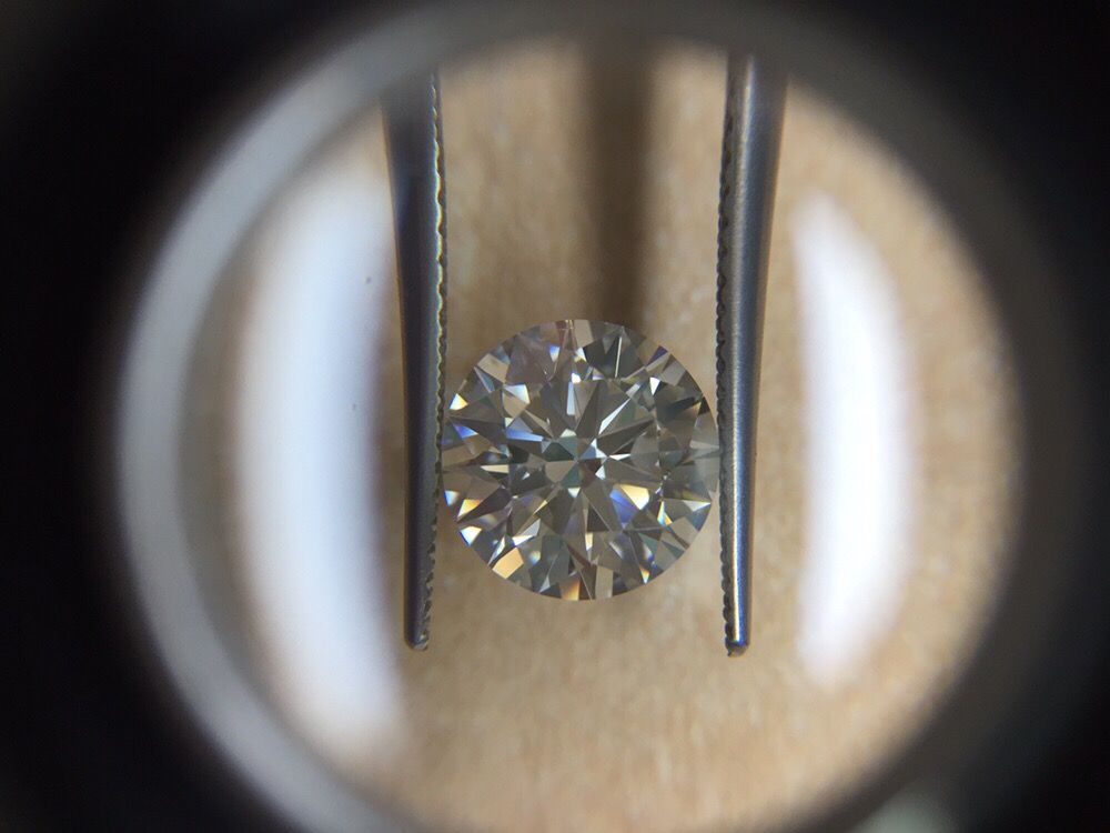 Diamond held by tweezers under magnification, centered on a beige background