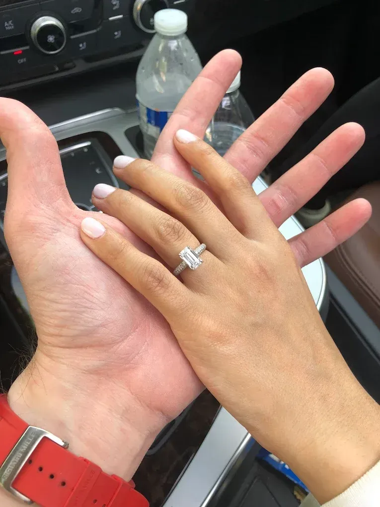 Two hands holding each other in a car, with a diamond ring visible on one hand.