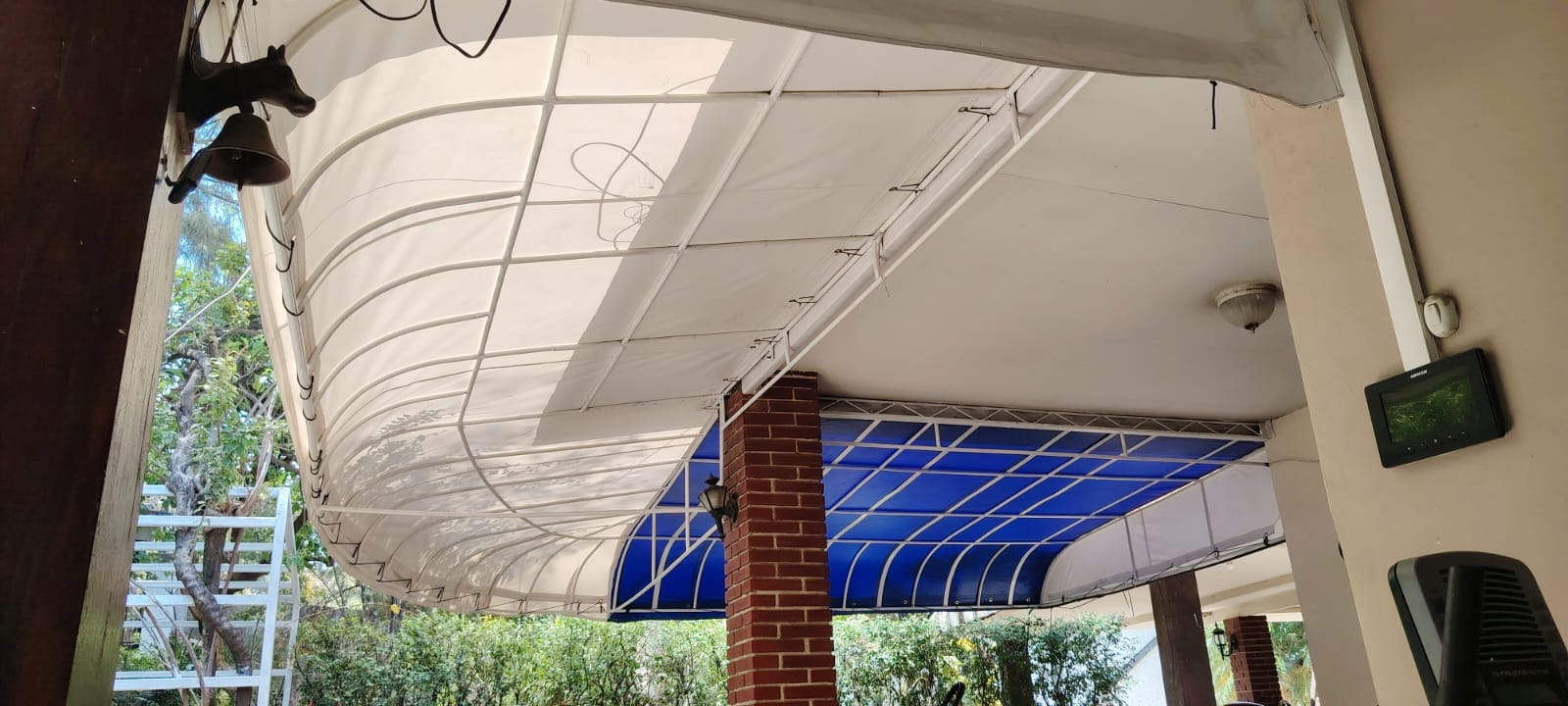 Vista exterior de un porche cubierto con techo curvo blanco, sostenido por ladrillos y pilares blancos.