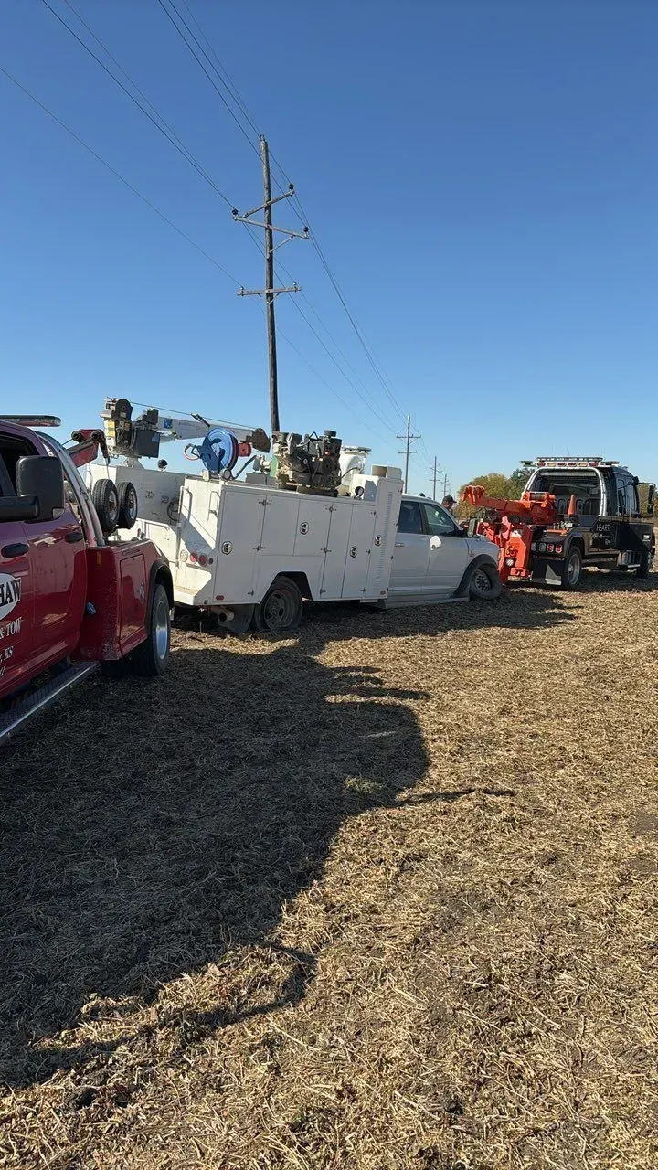 A red tow truck and a white service utility truck parked in a harvested field under a clear blue sky.