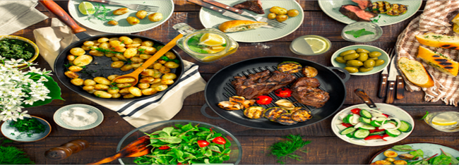 Et træbord fyldt med en række forskellige retter, herunder kartofler, salat, kød og oliven.