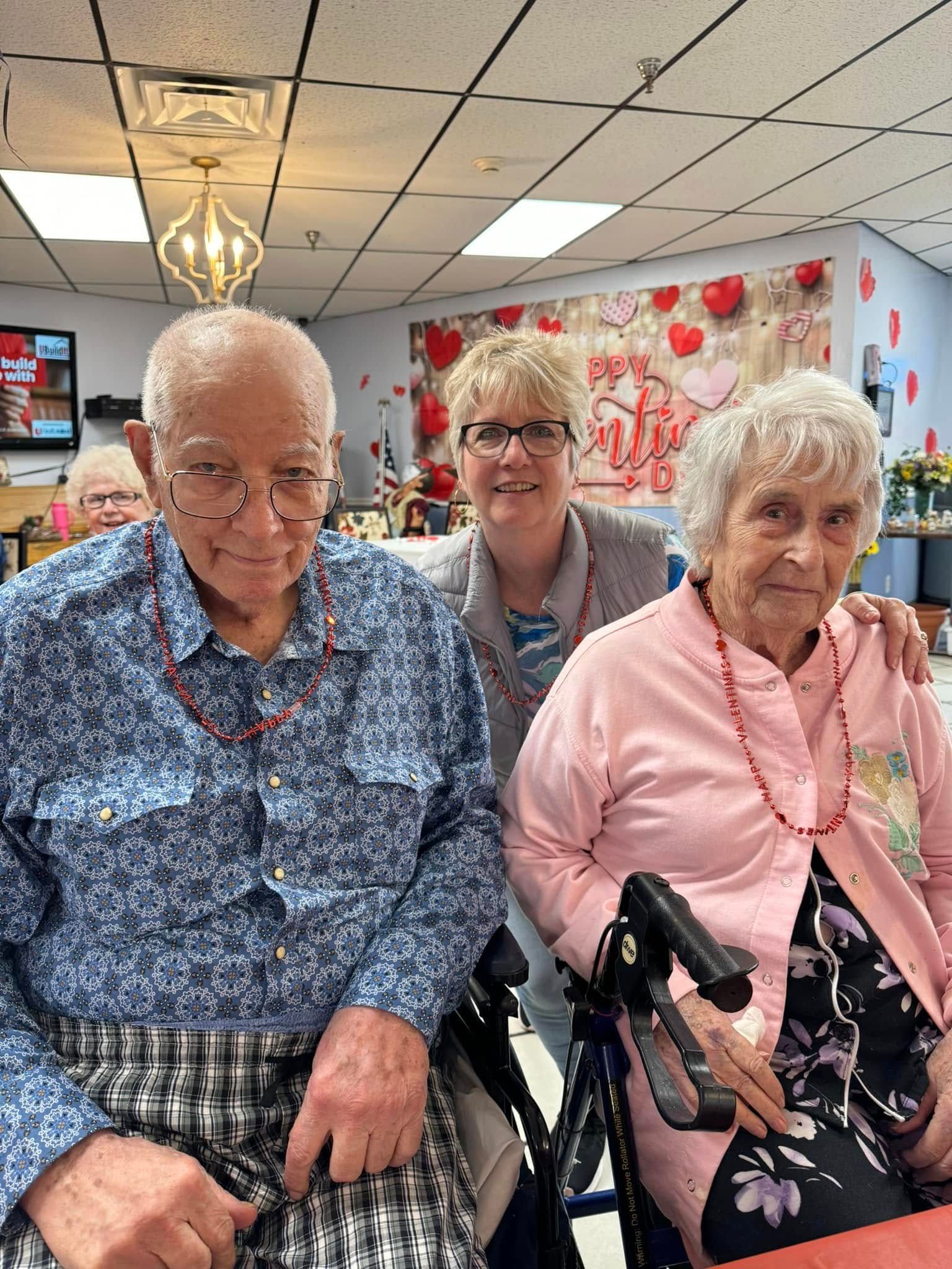 Elderly couple with woman between them; Valentine's Day decorations in background; smiling.