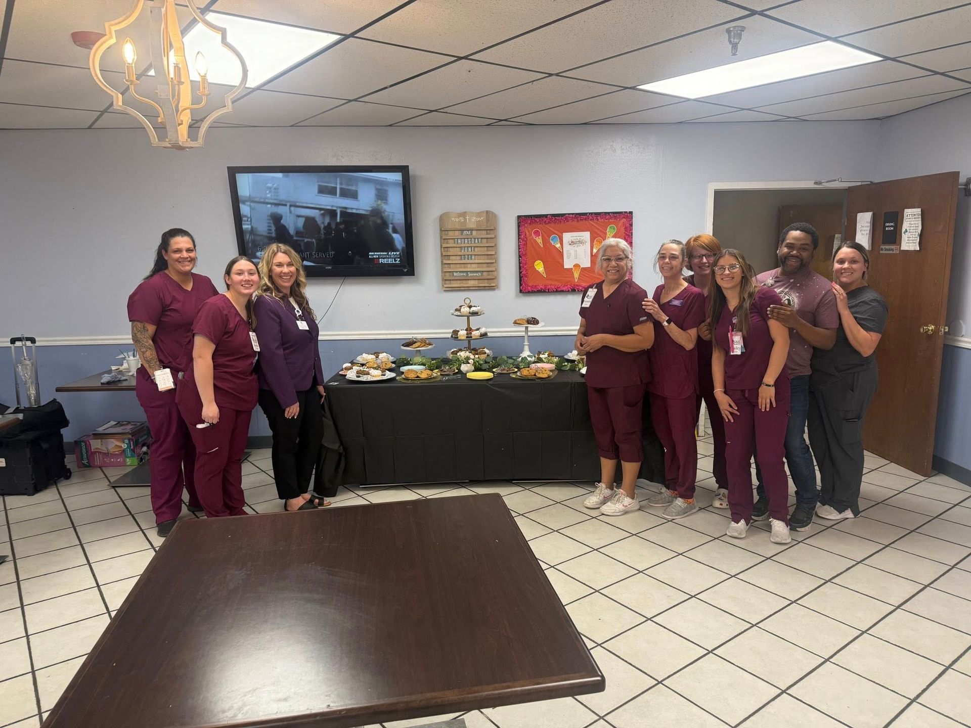 A group of people in burgundy scrubs pose together in a room with food on a table.