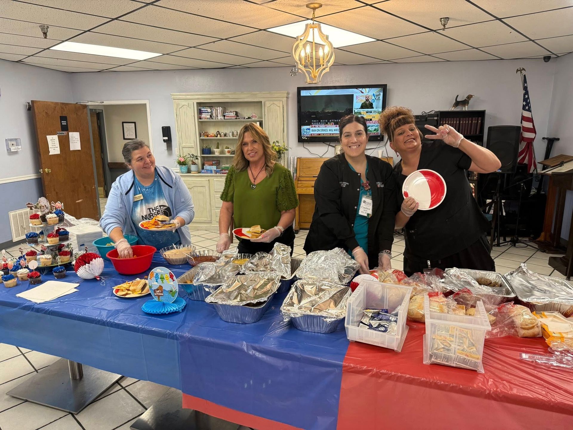 Four healthcare workers at a buffet table with food. Red, white, and blue decorations.