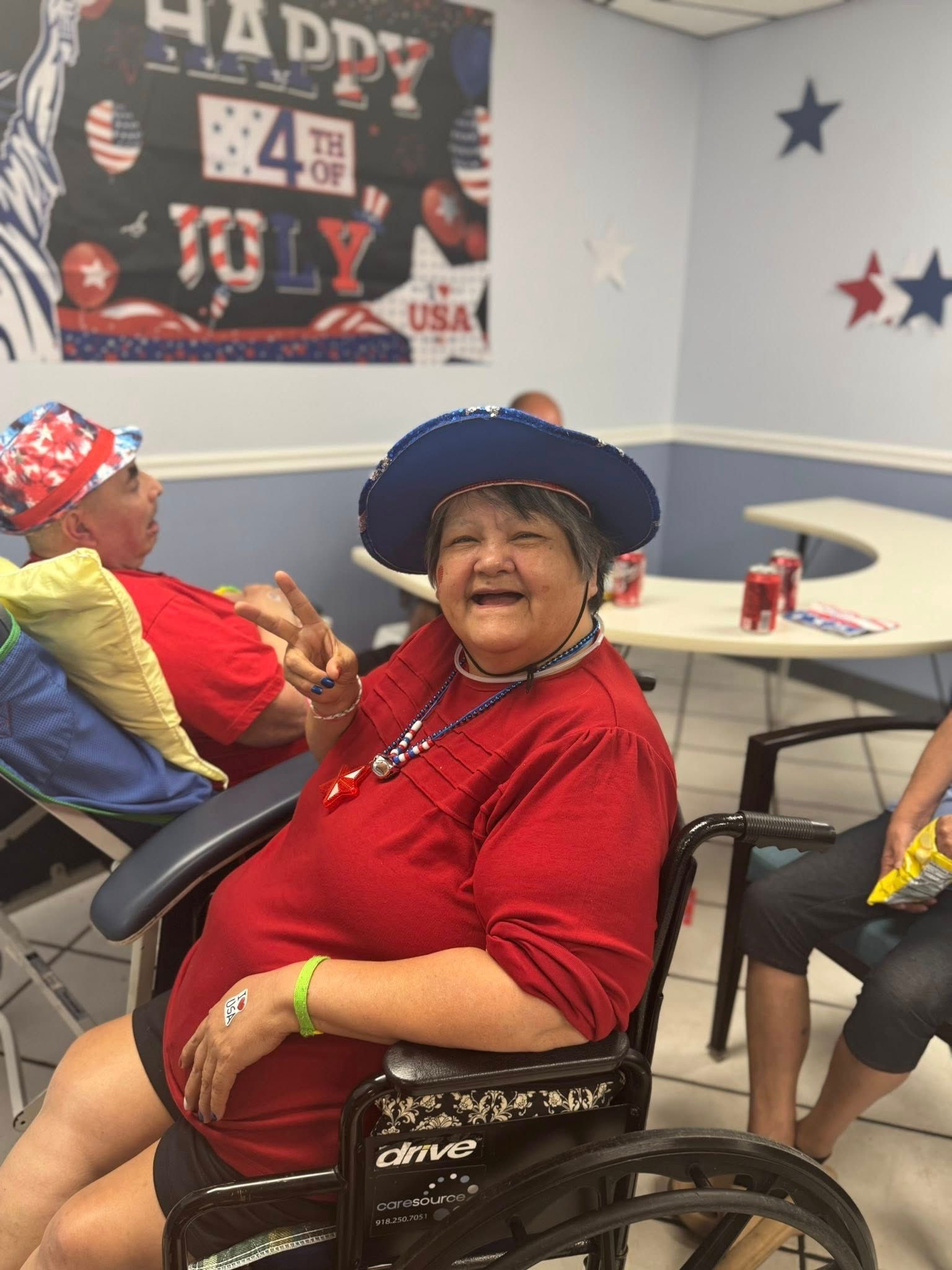 Woman in red, white, and blue, smiling, seated in a wheelchair, celebrating July 4th.