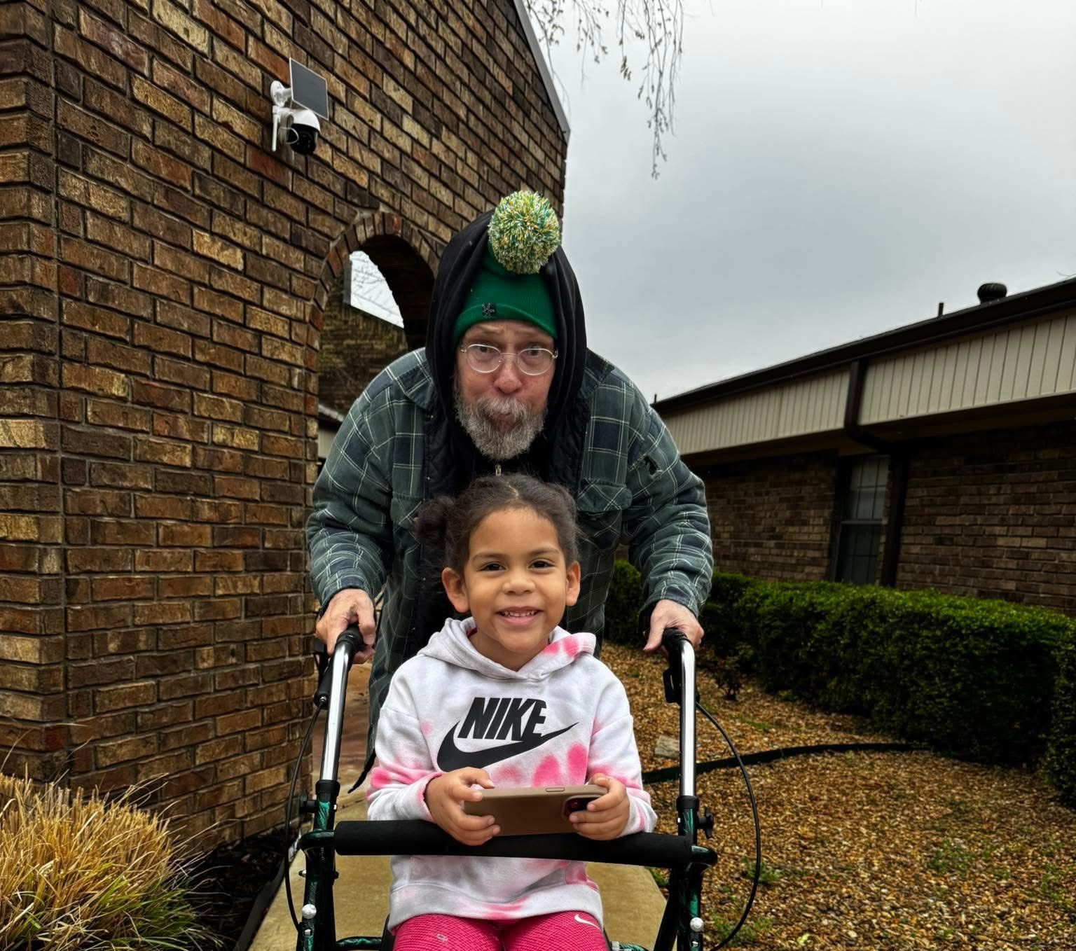 Person holding pink dumbbells, exercising indoors, another person in the background.