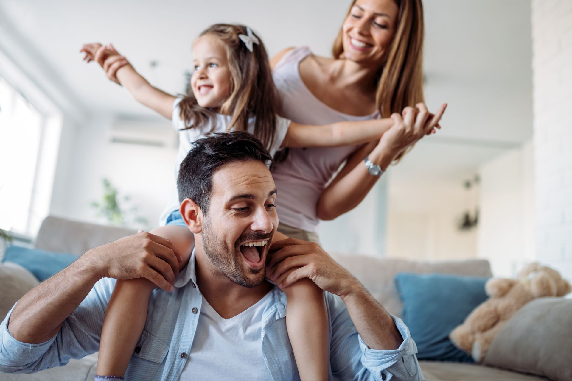 A man is carrying a little girl on his shoulders in a living room.