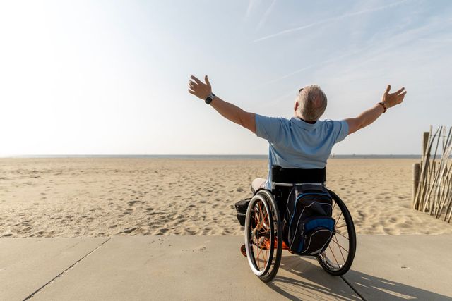 A man in a wheelchair is standing on the beach with his arms outstretched. A man in a wheelchair is standing on the beach with his arms outstretched.