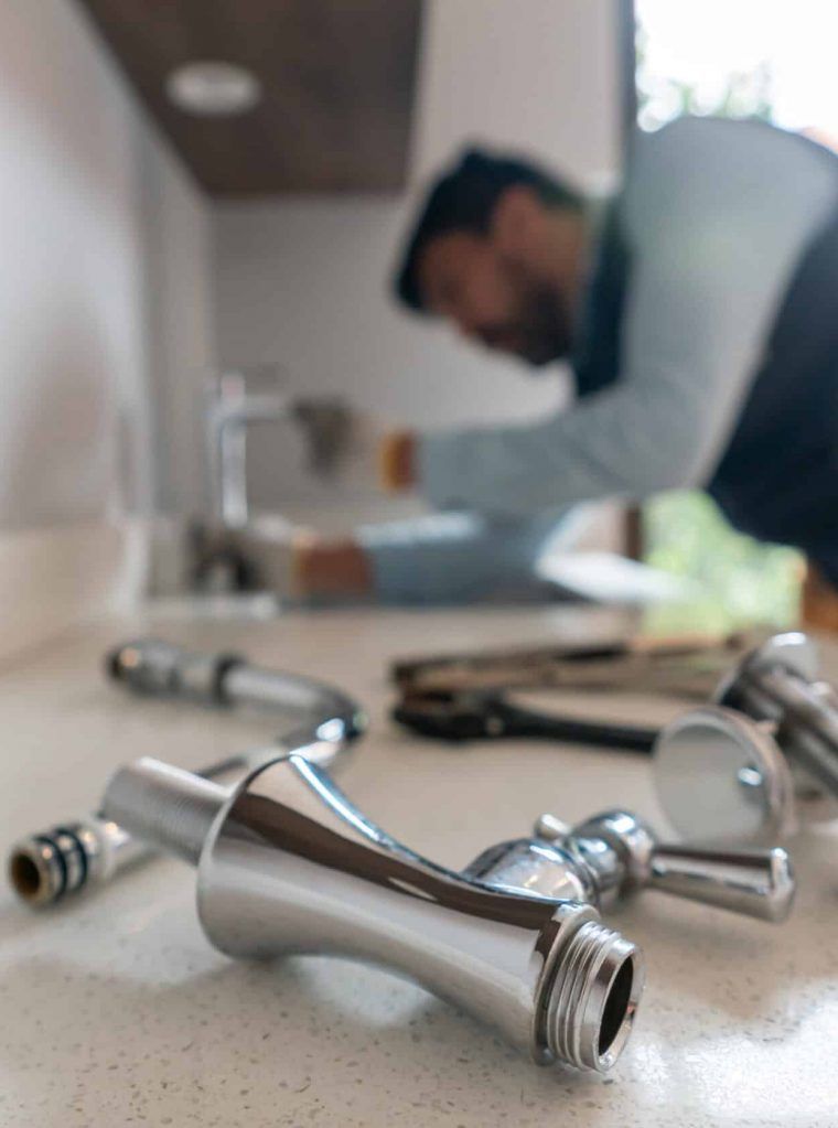 Un plombier répare un robinet, ses outils éparpillés sur le plan de travail.