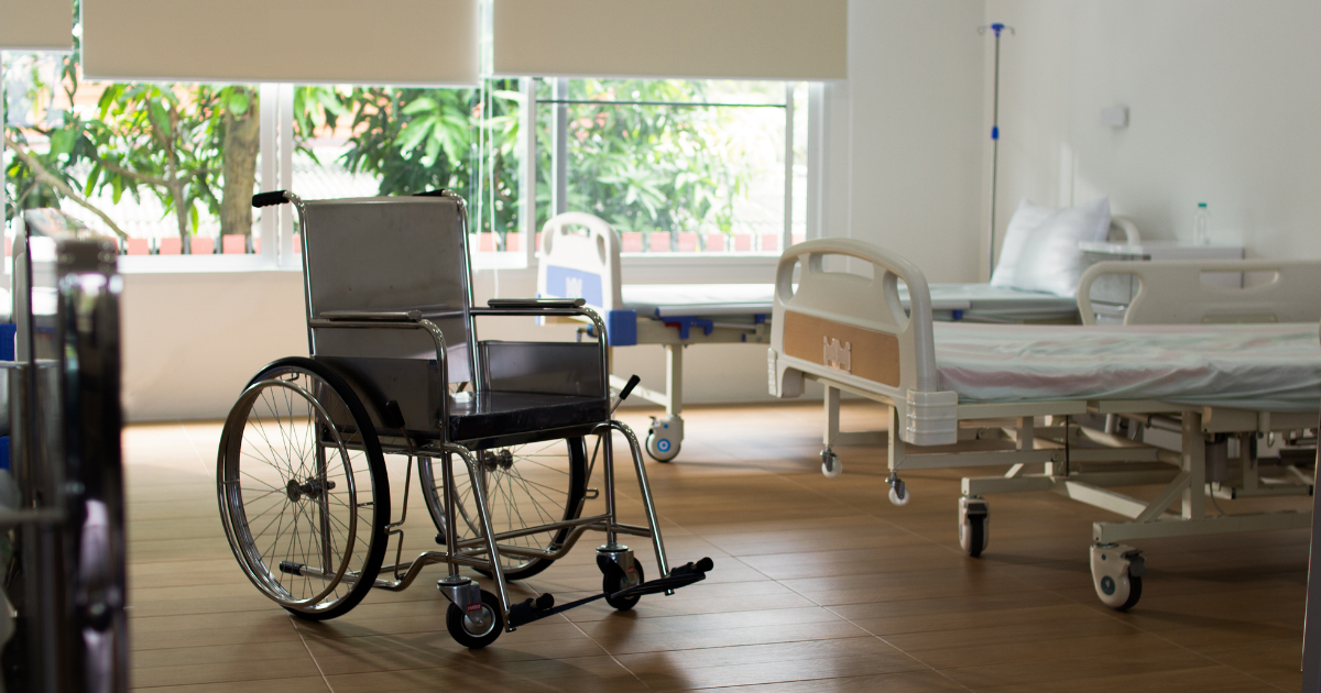 A nursing home room with two hospital beds and a wheelchair