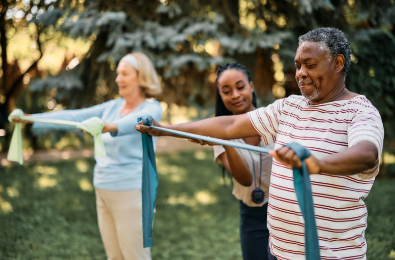 Woman assists two older adults with resistance band exercises