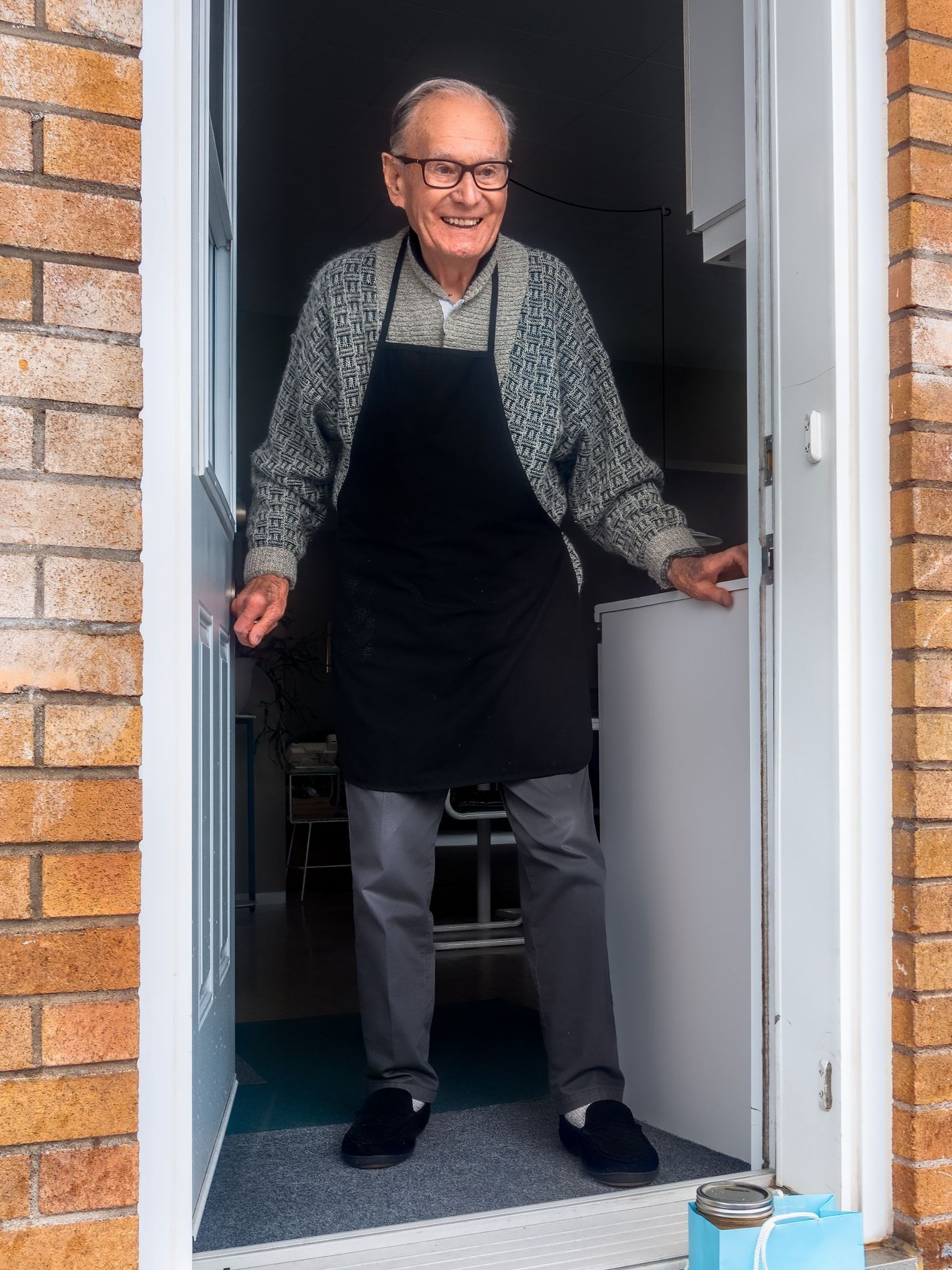 an elderly man in an apron is standing in a doorway .