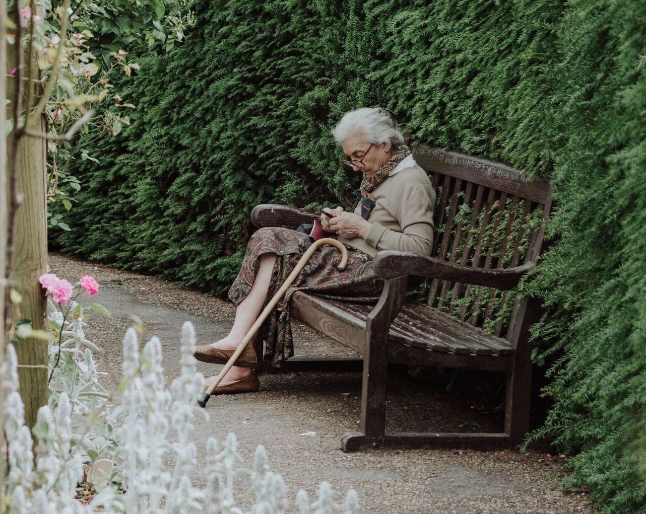 an elderly woman is sitting on a bench looking at her phone .