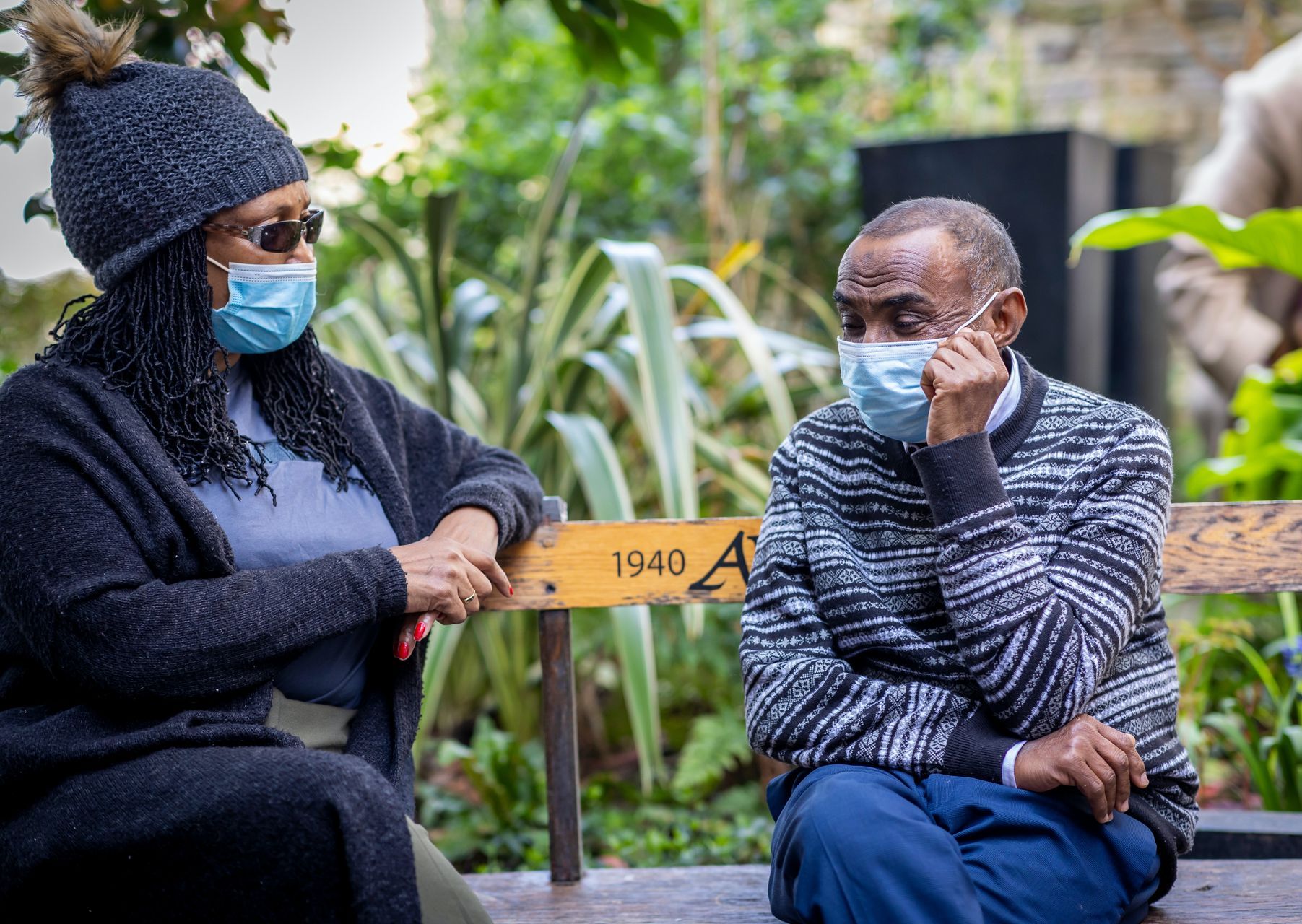 a man and a woman wearing face masks are sitting on a bench .