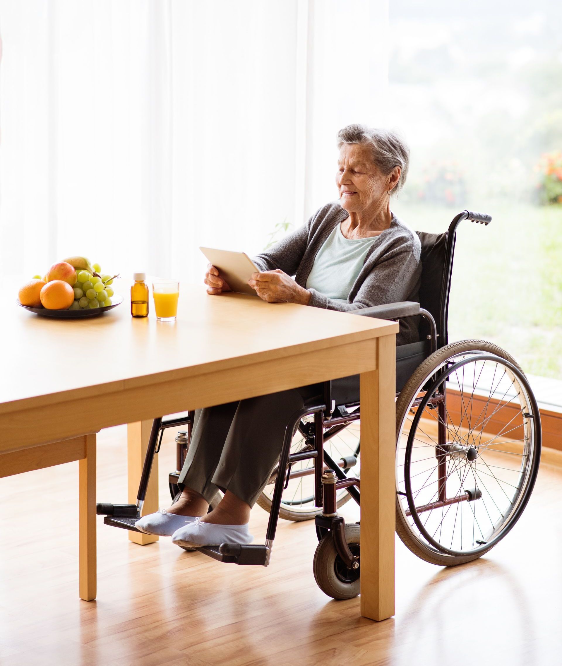 an elderly woman in a wheelchair is sitting at a table using a tablet .