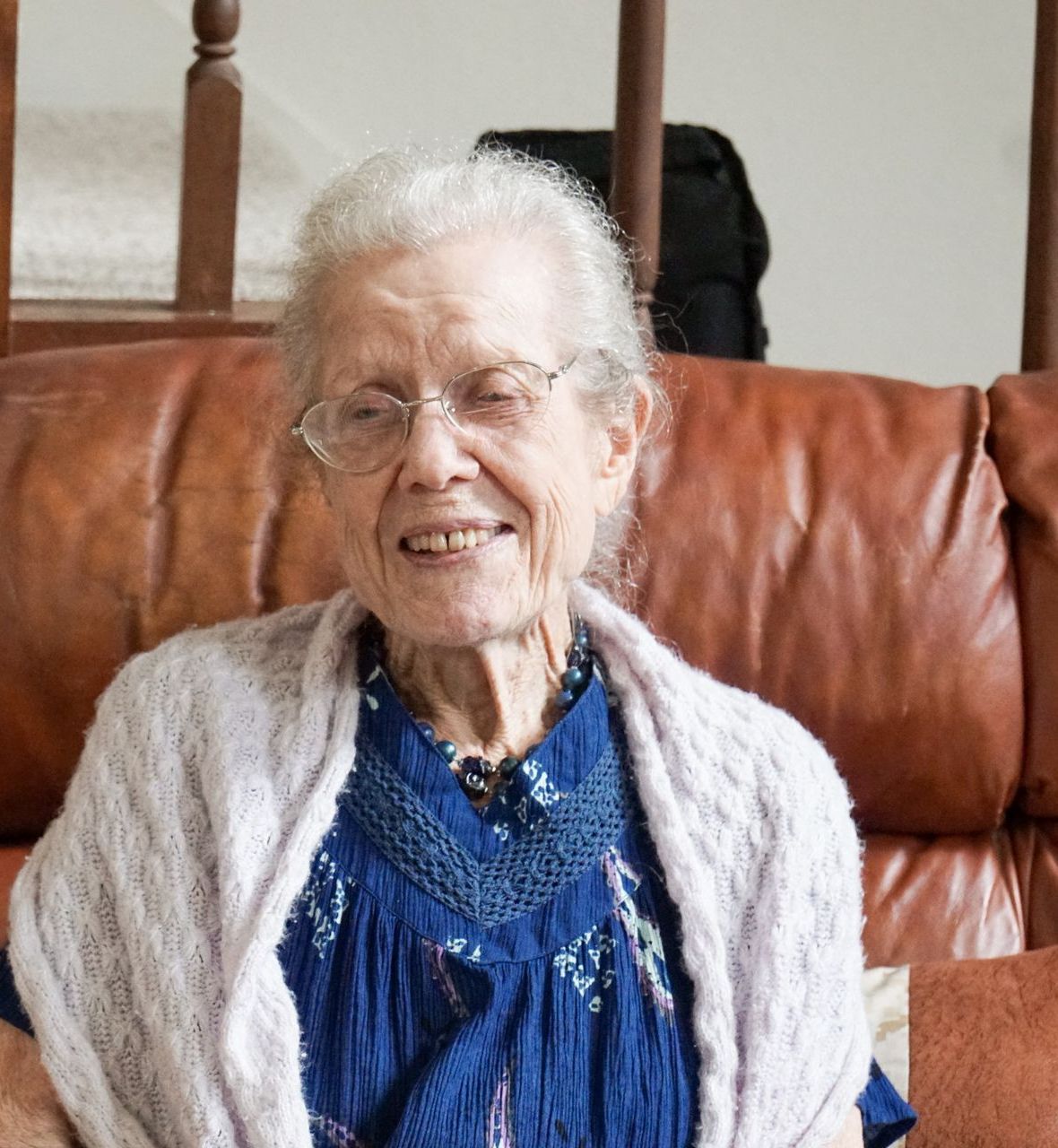 an elderly woman wearing glasses and a blue shirt is sitting on a couch