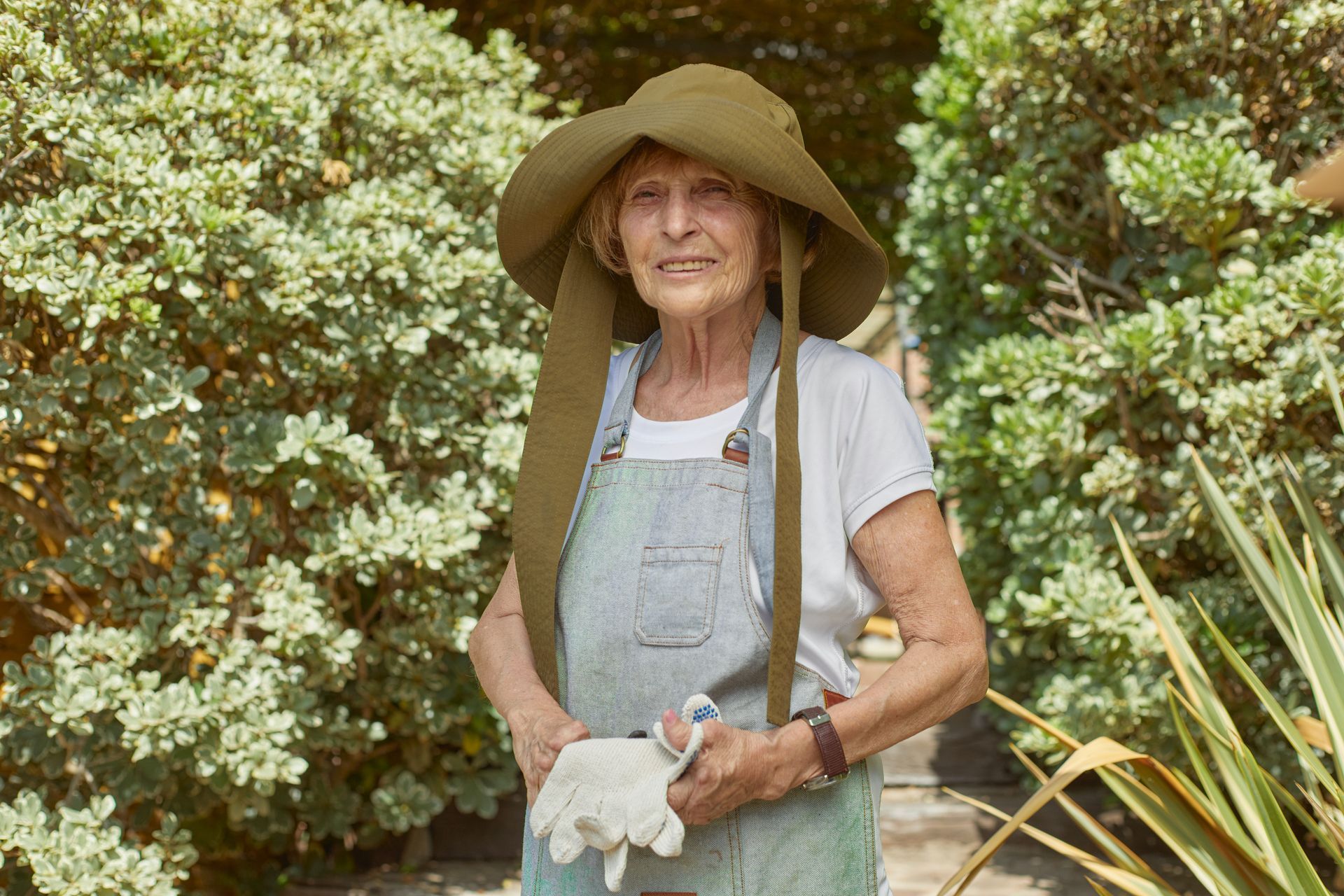 an elderly woman wearing a hat and apron is standing in a garden .