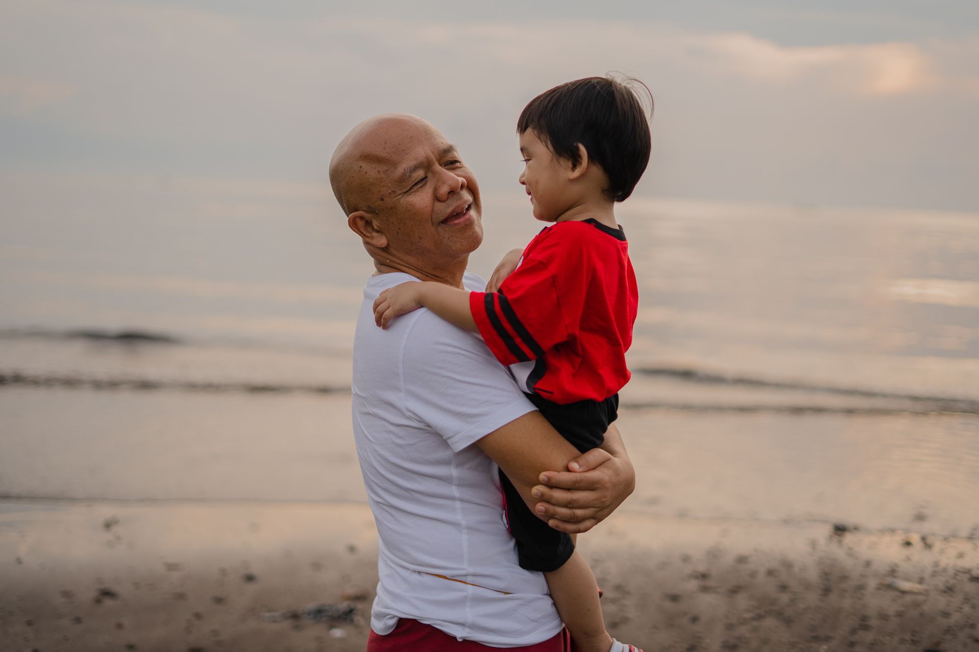 a man is holding a little boy on his shoulders on the beach .