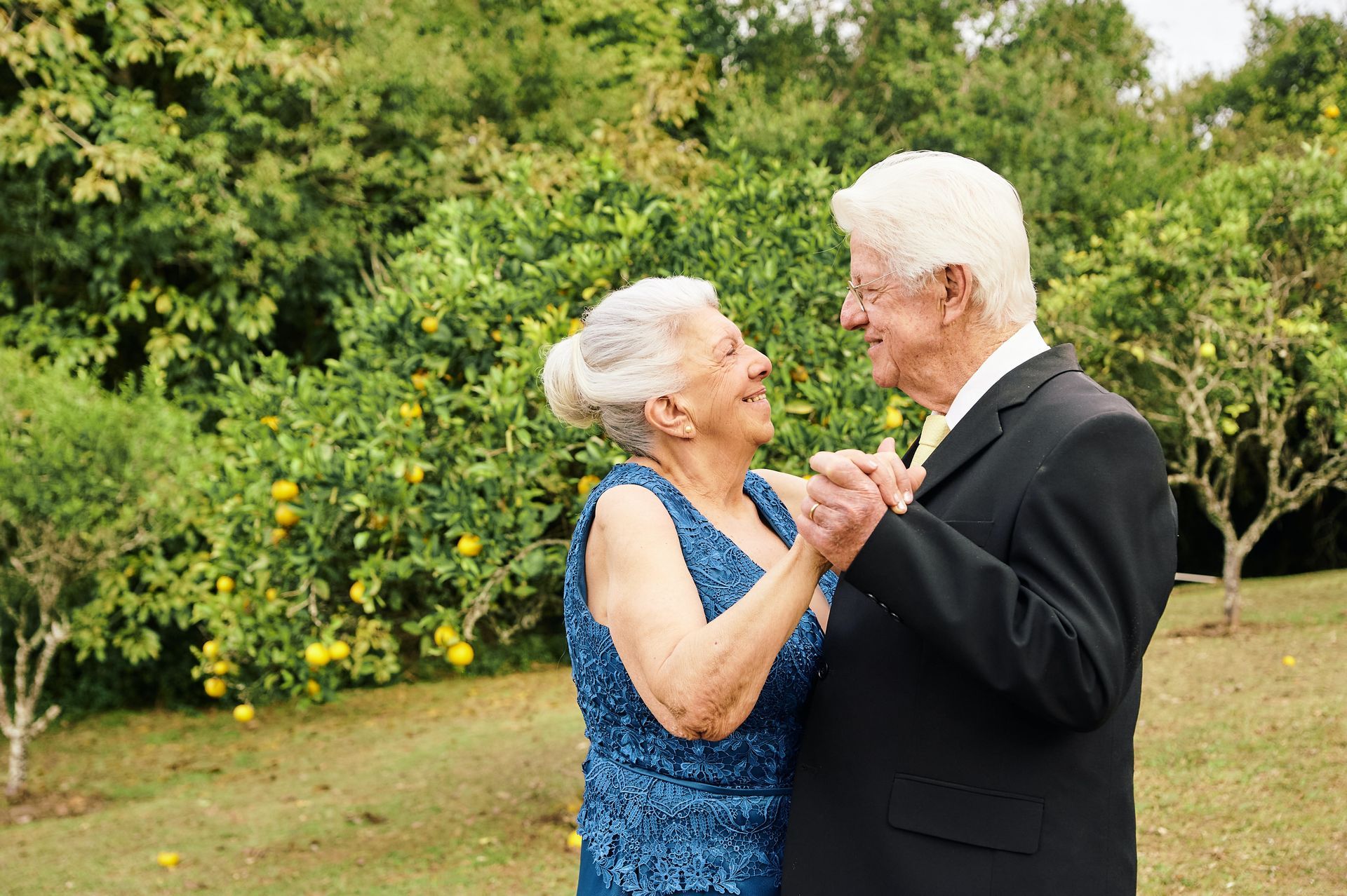an elderly couple is dancing together in a park .