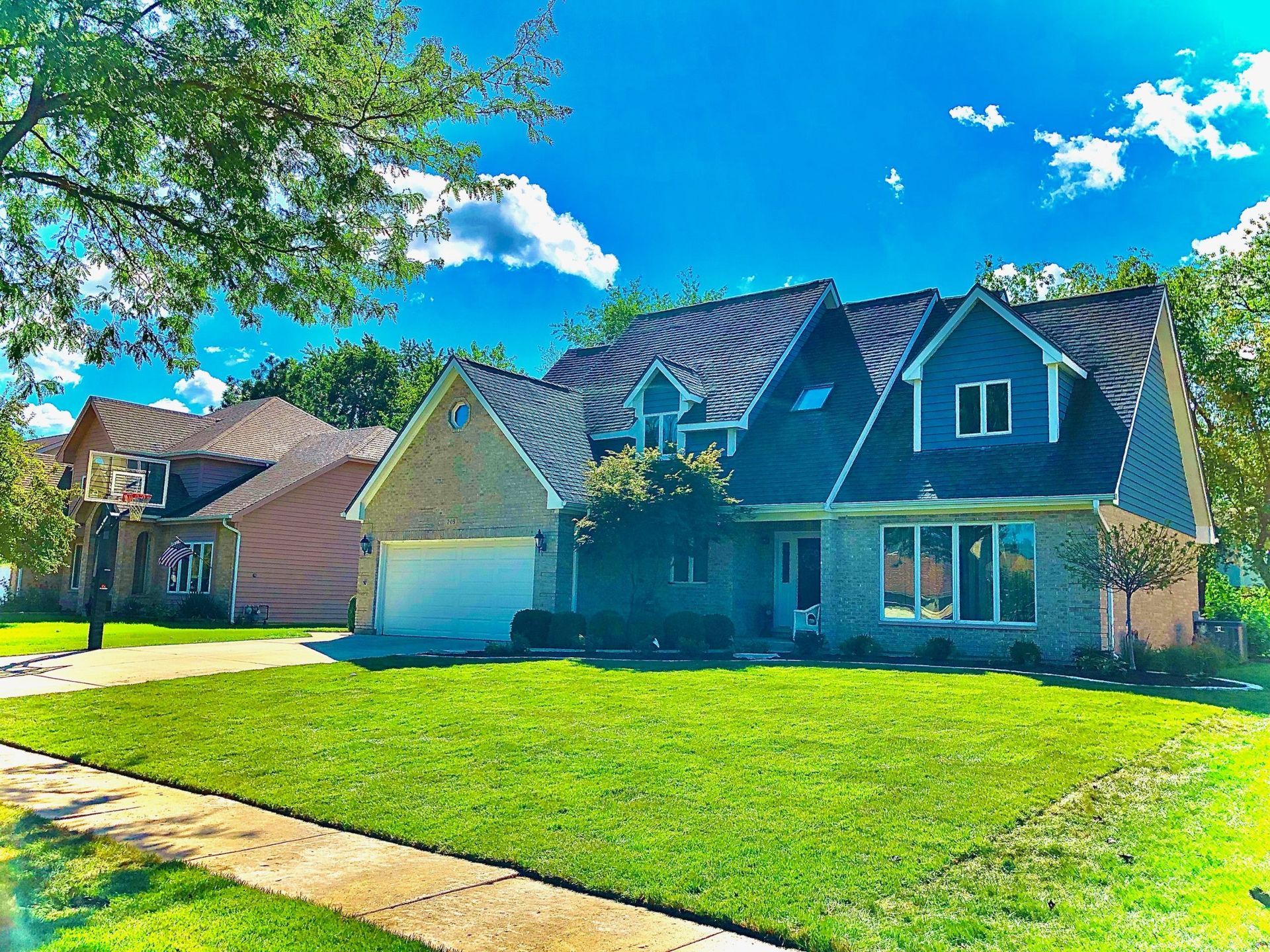 Two-story houses with green lawns, trees, and a bright blue sky.