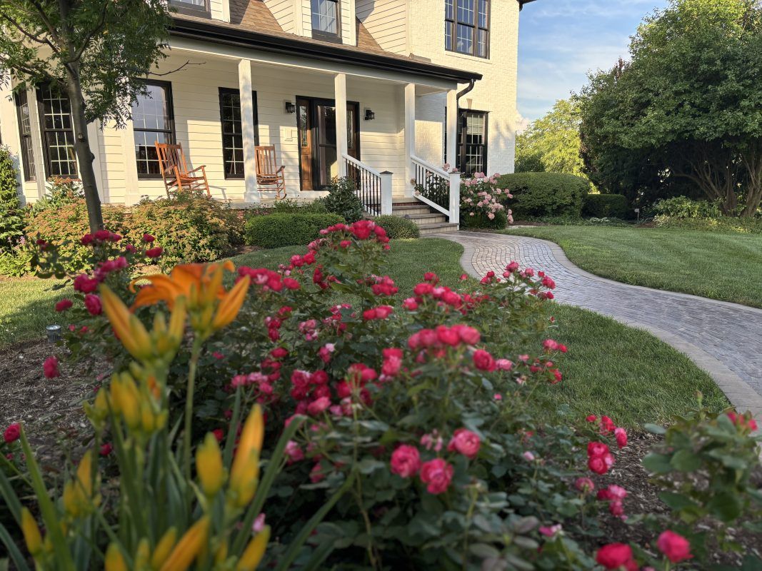 White house with black trim, surrounded by a vibrant flower garden and a brick pathway leading to the front door.