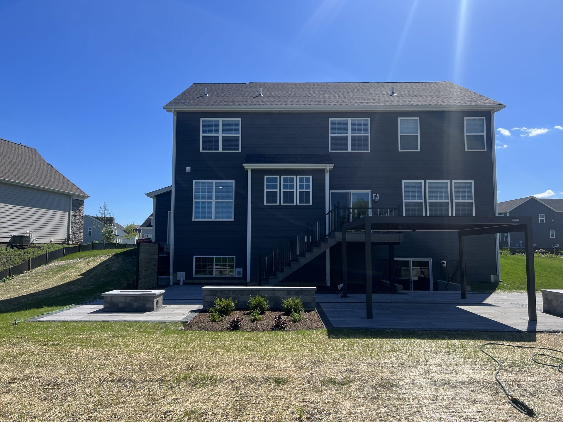 Dark blue house with a patio, fire pit, and pergola under a bright blue sky.