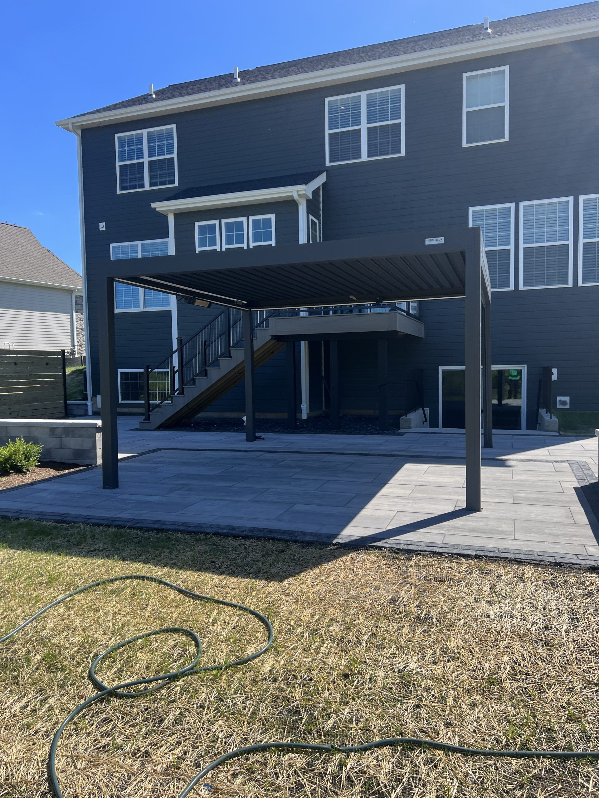 A black pergola over a gray patio outside a two-story blue house.