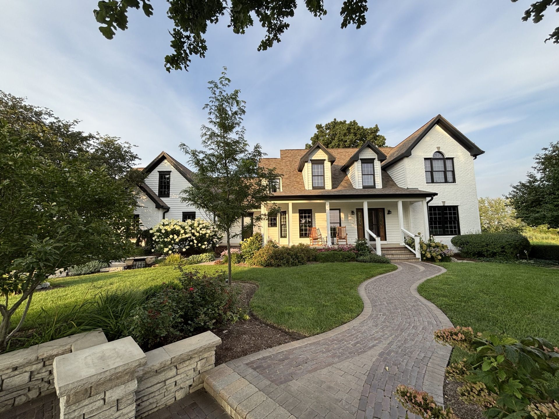 White farmhouse with black trim, a curved stone walkway, and lush landscaping.