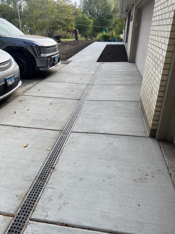 Concrete driveway with drainage grate, bordering a garage and parked cars.