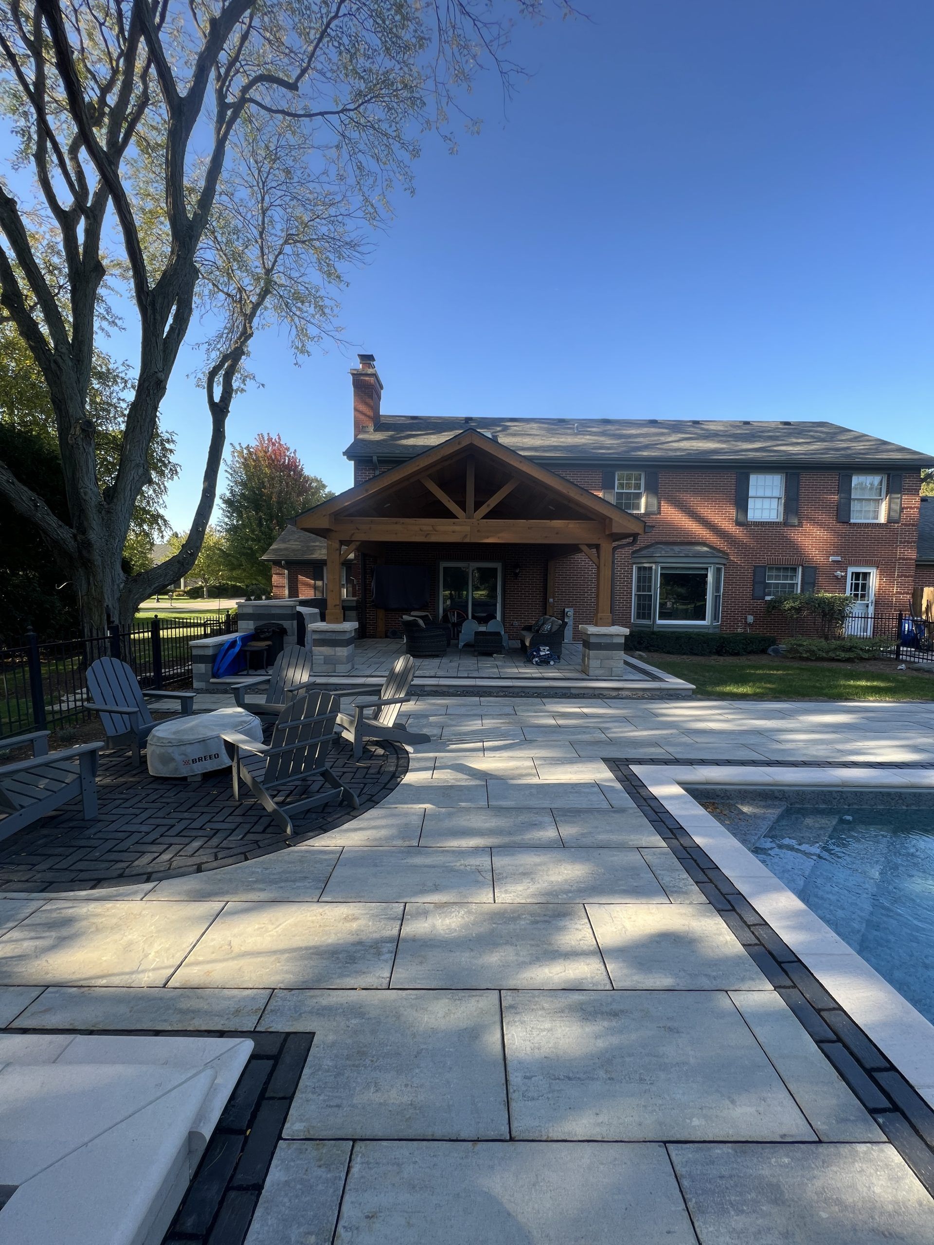 Backyard with pool, patio, and wooden covered seating area in front of a wood-sided house.