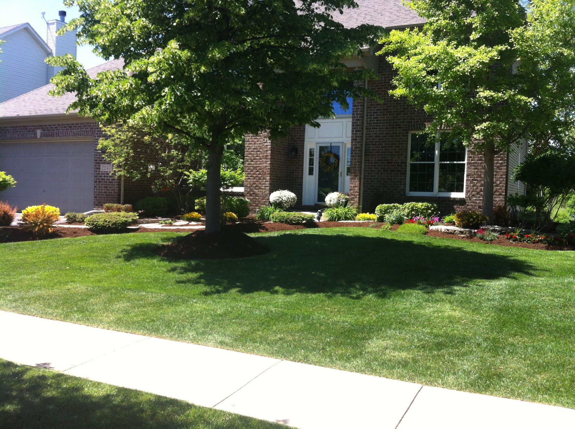 House with brick facade, lush green lawn, trees, and landscaping along the front.