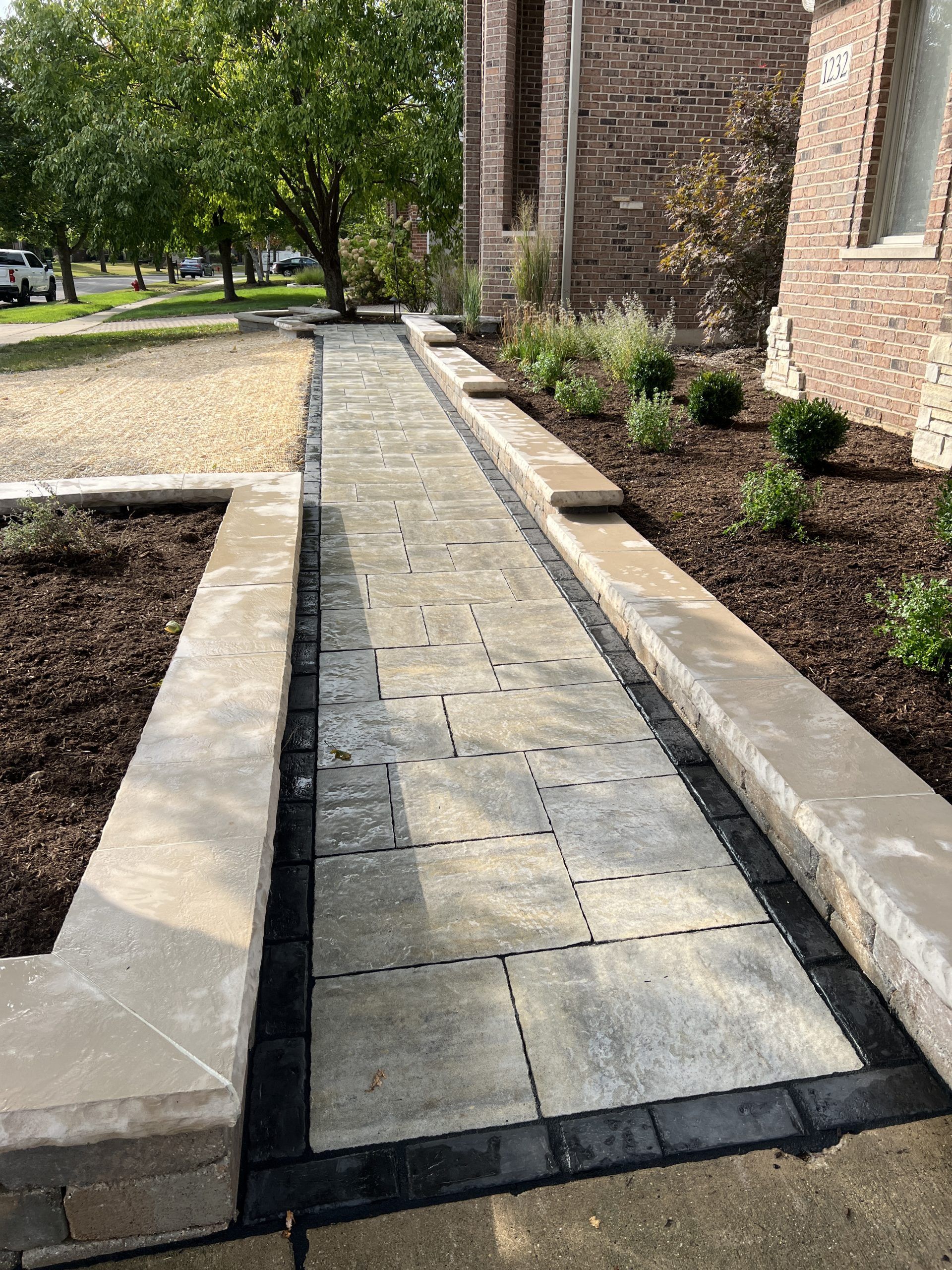 Stone pathway with low retaining walls, leading to a brick building.