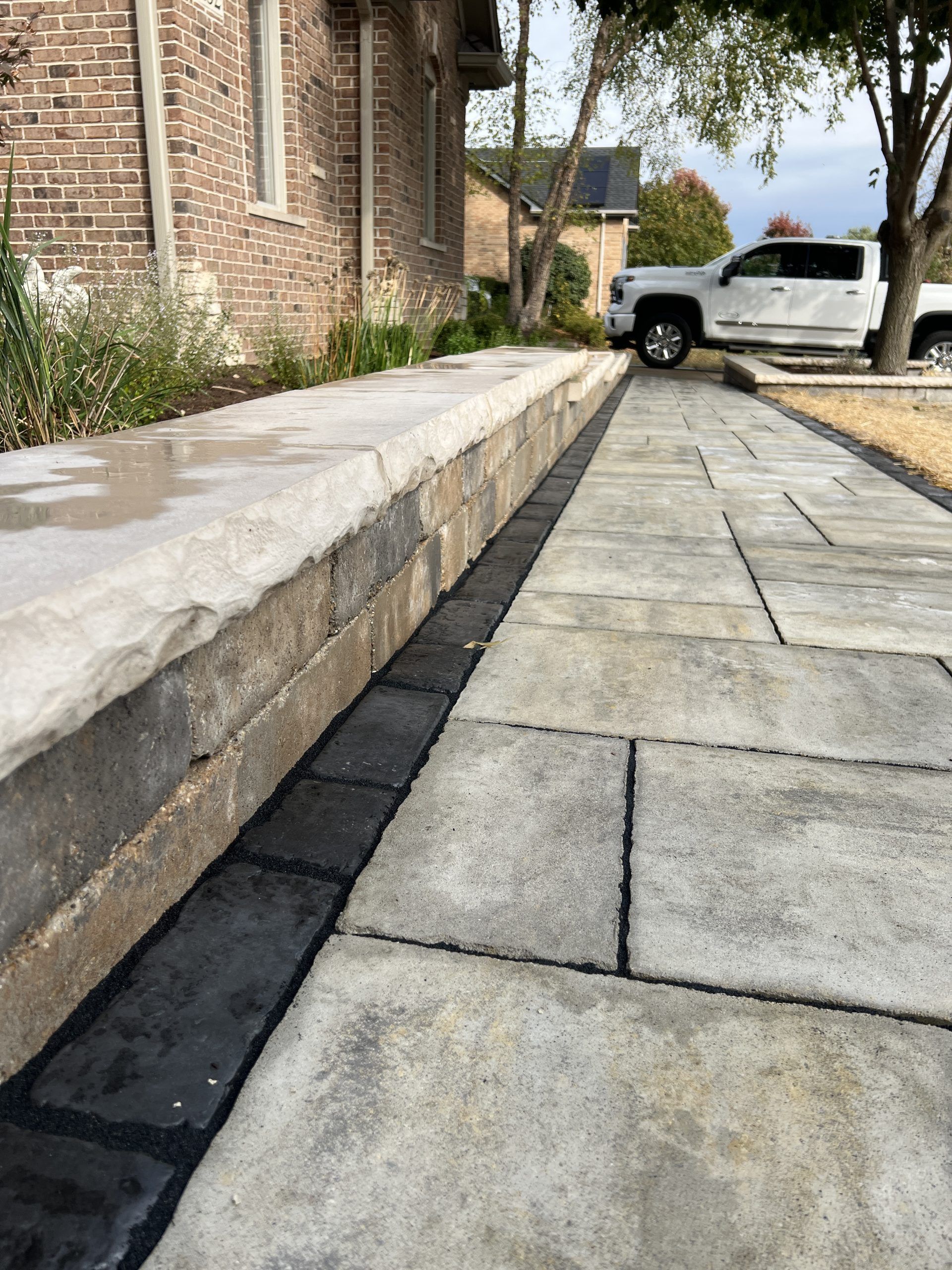 Stone walkway with a low wall alongside a building, and a truck parked in the background.