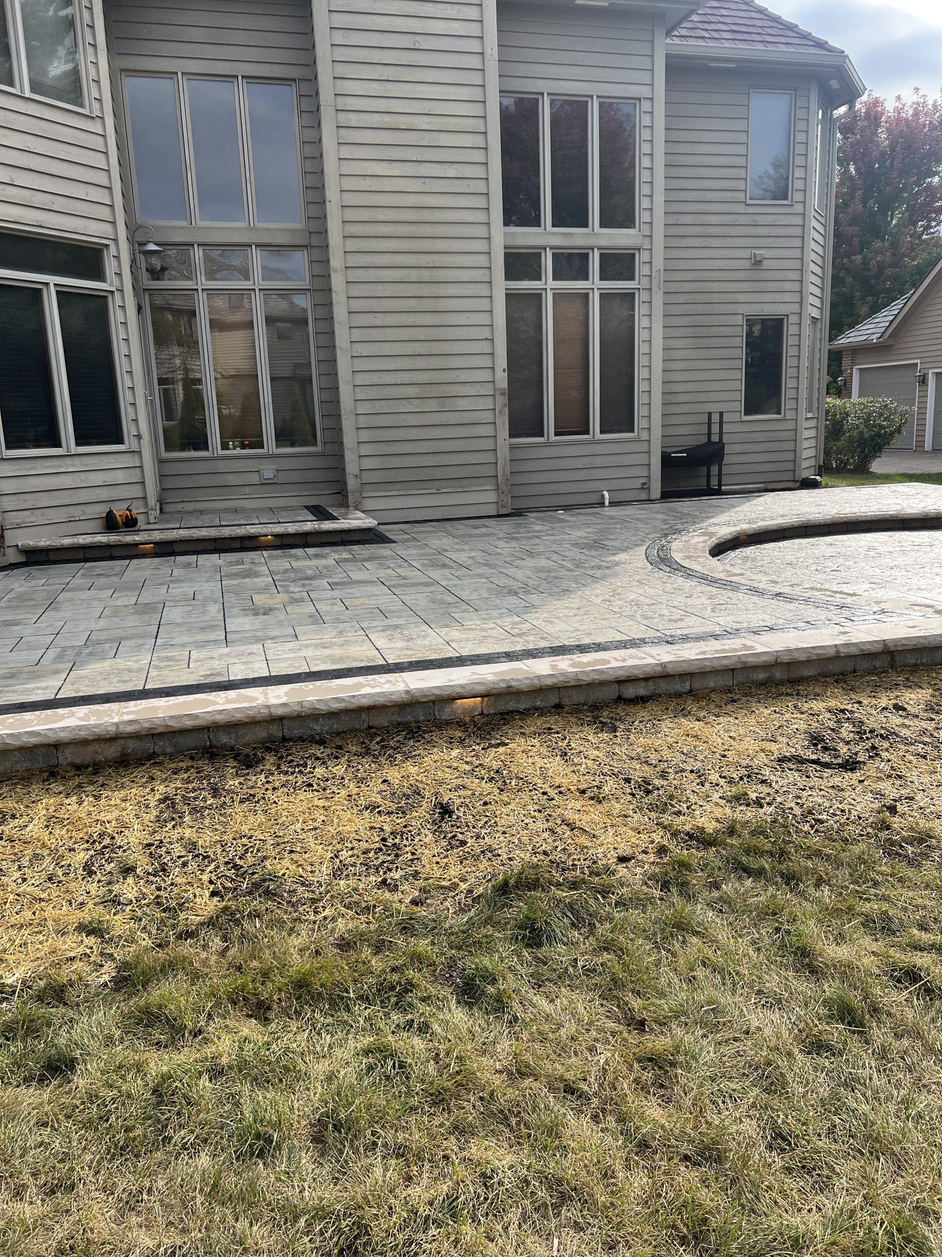 Back of a two-story beige house with large windows, adjacent to a stone patio and grassy yard.
