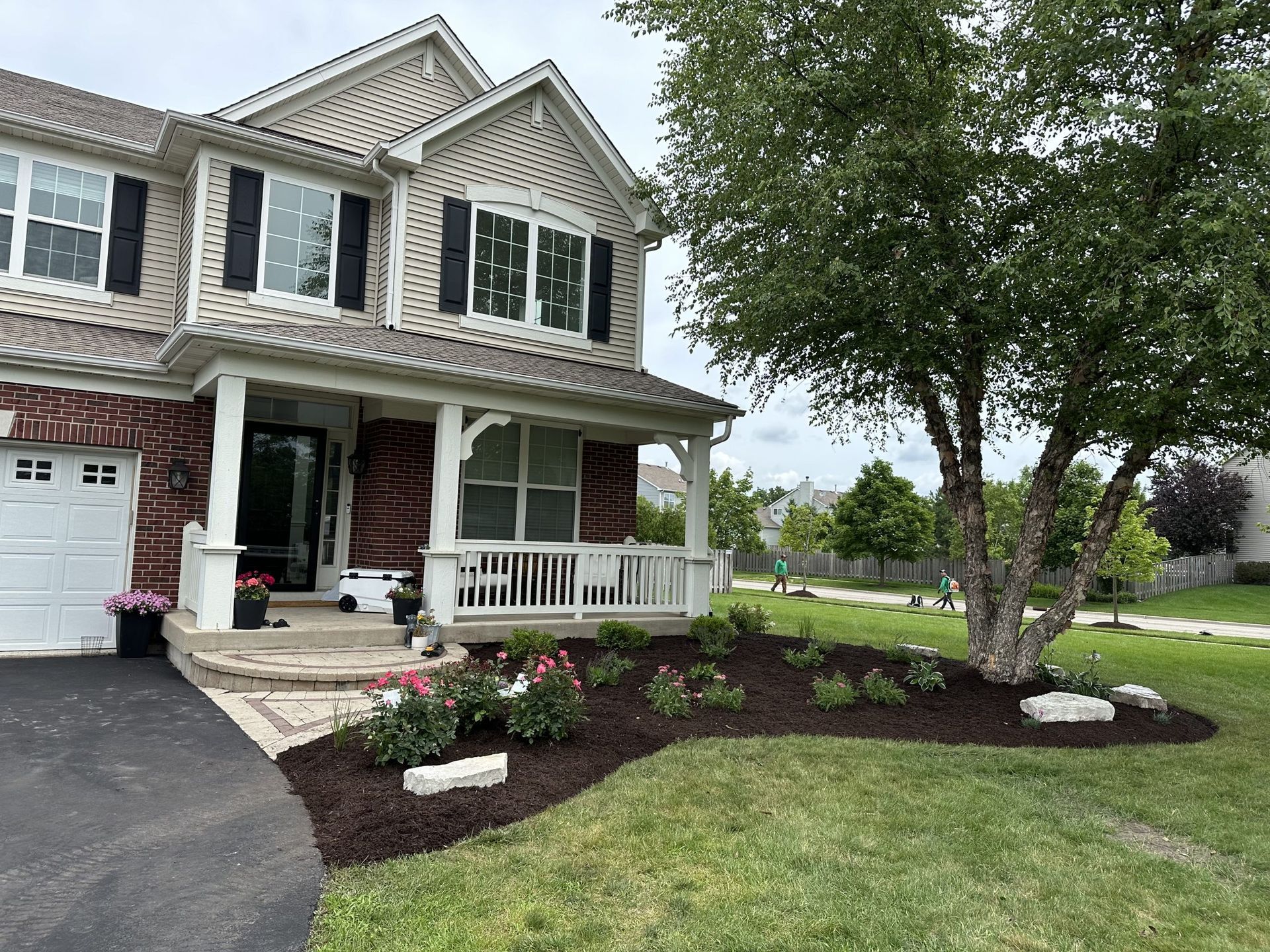 Two-story house with a porch, surrounded by a lawn and landscaped flower beds with a birch tree.
