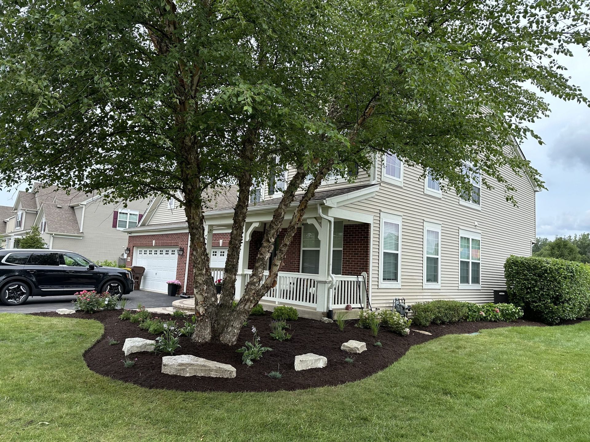 A two-story house with a porch, a large tree in the front yard, and landscaping.