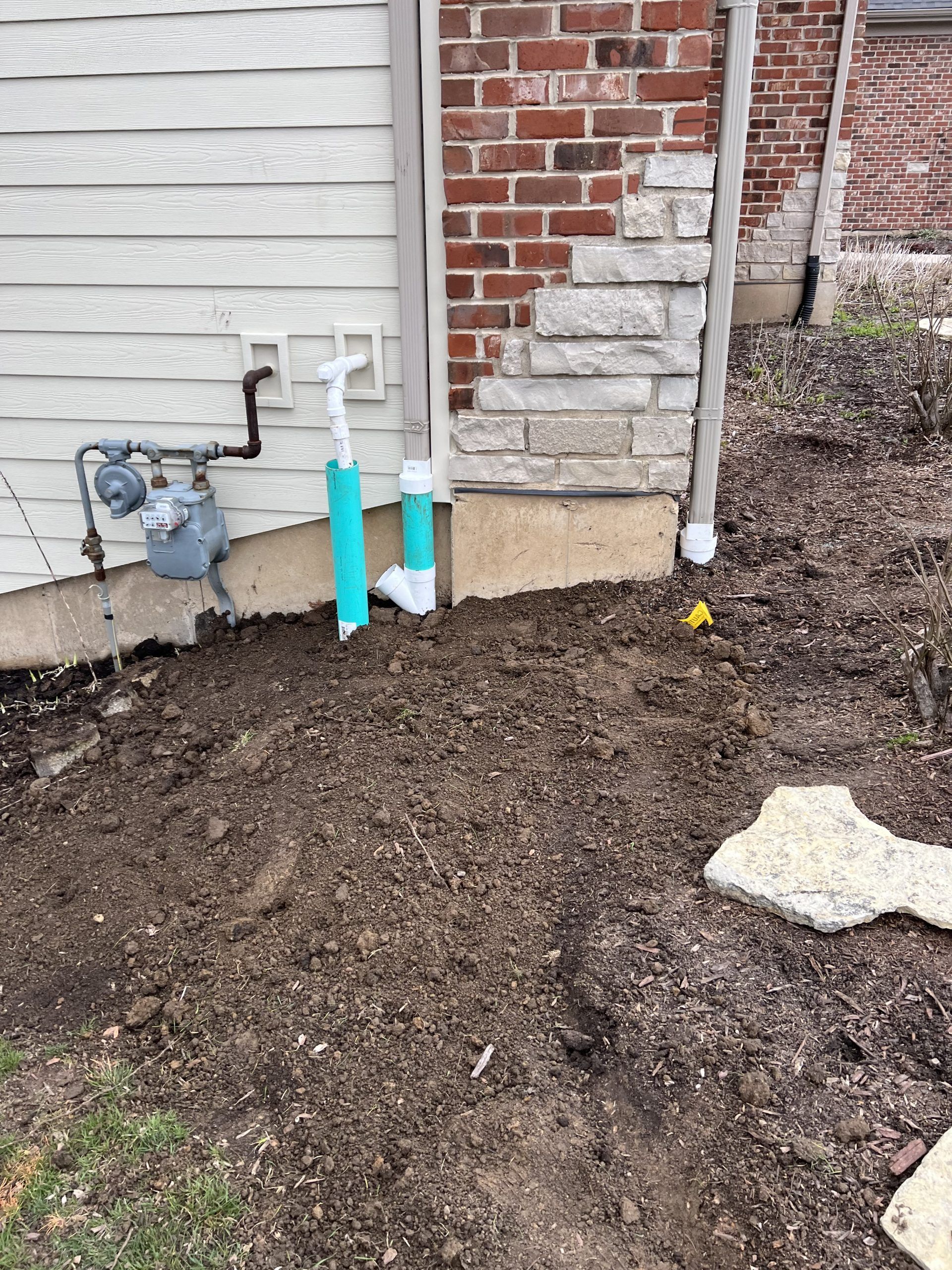Exterior of a building with gas meter, exposed pipes, and excavated ground.