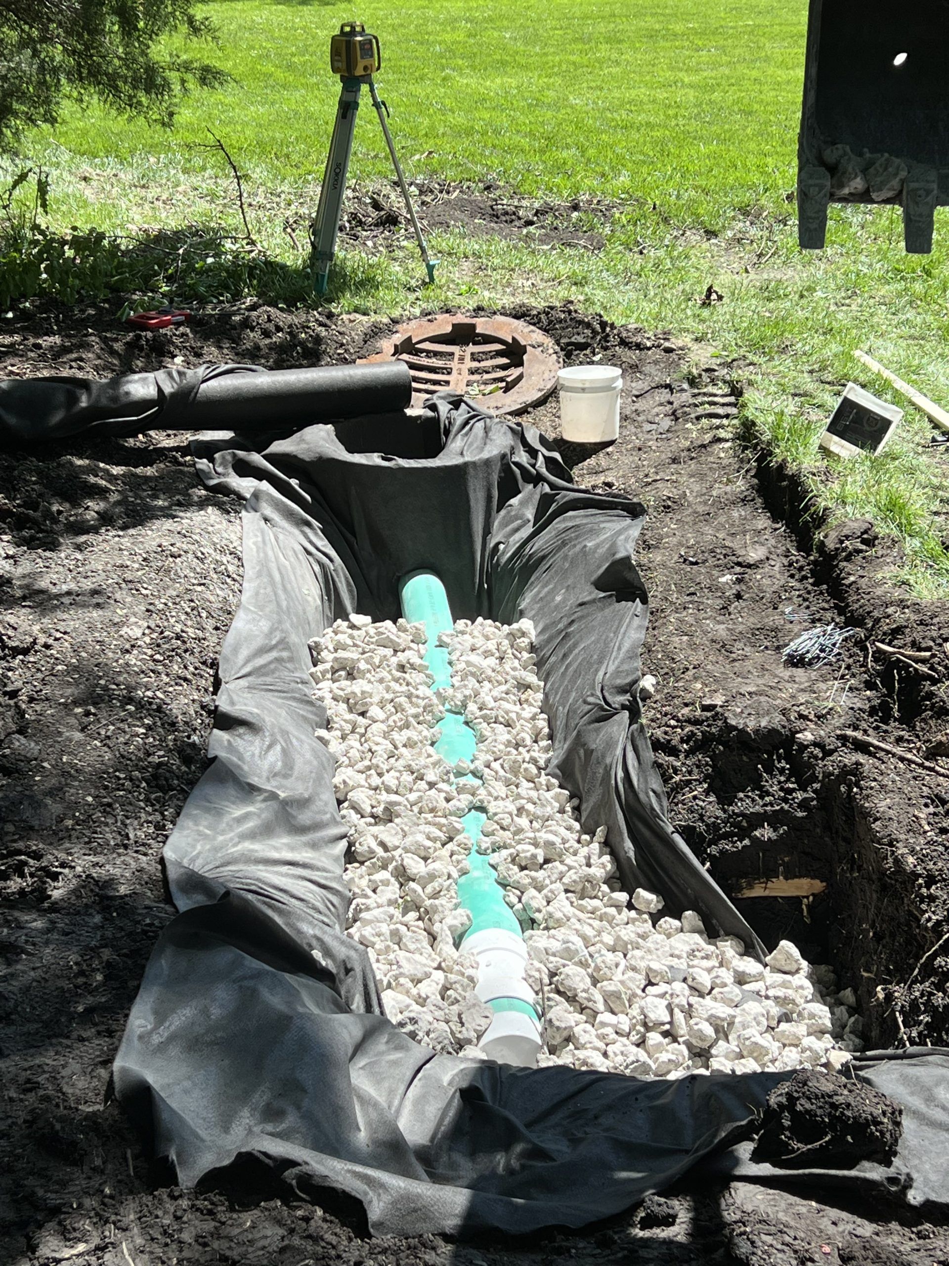 A trench filled with gravel and a perforated pipe, part of a drainage system installation outdoors.