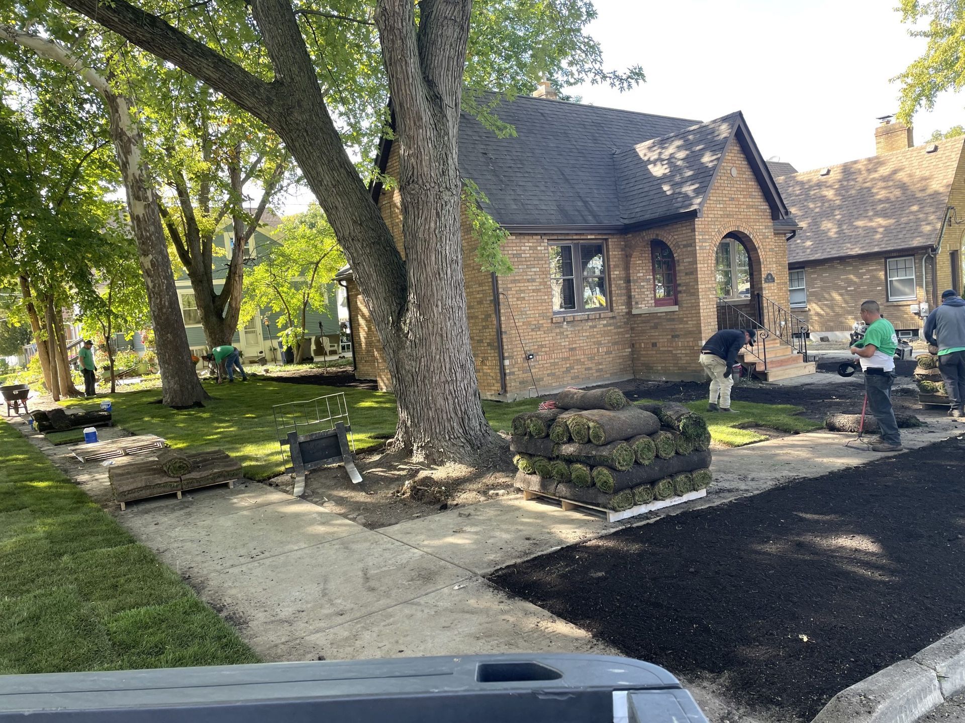 Workers install sod and landscaping near a brick house on a sunny day.