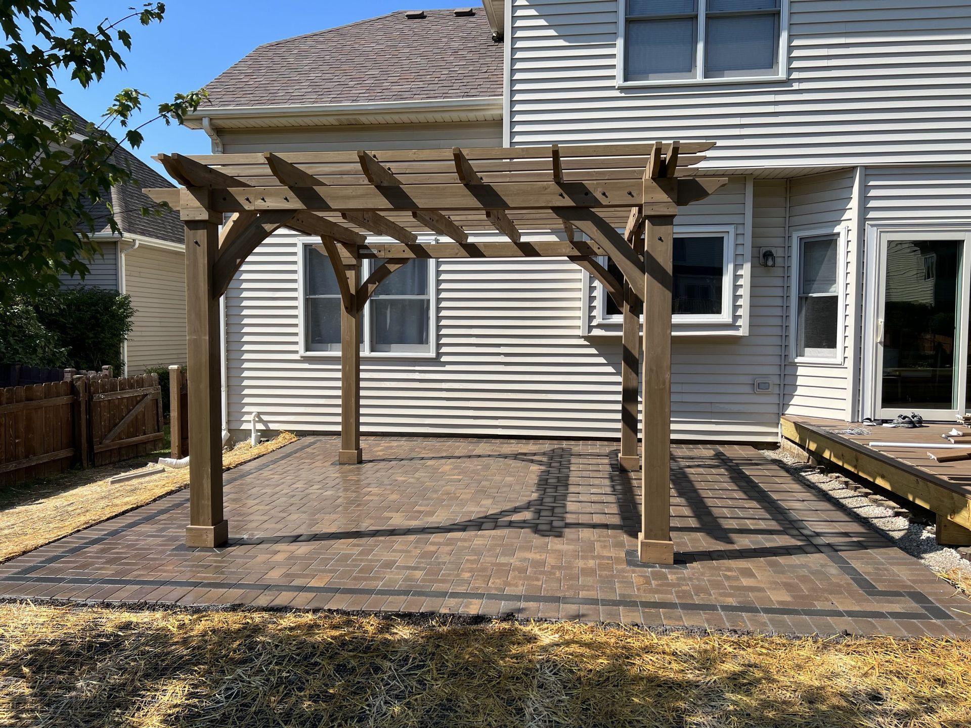 Wooden pergola on a brick patio in front of a house.